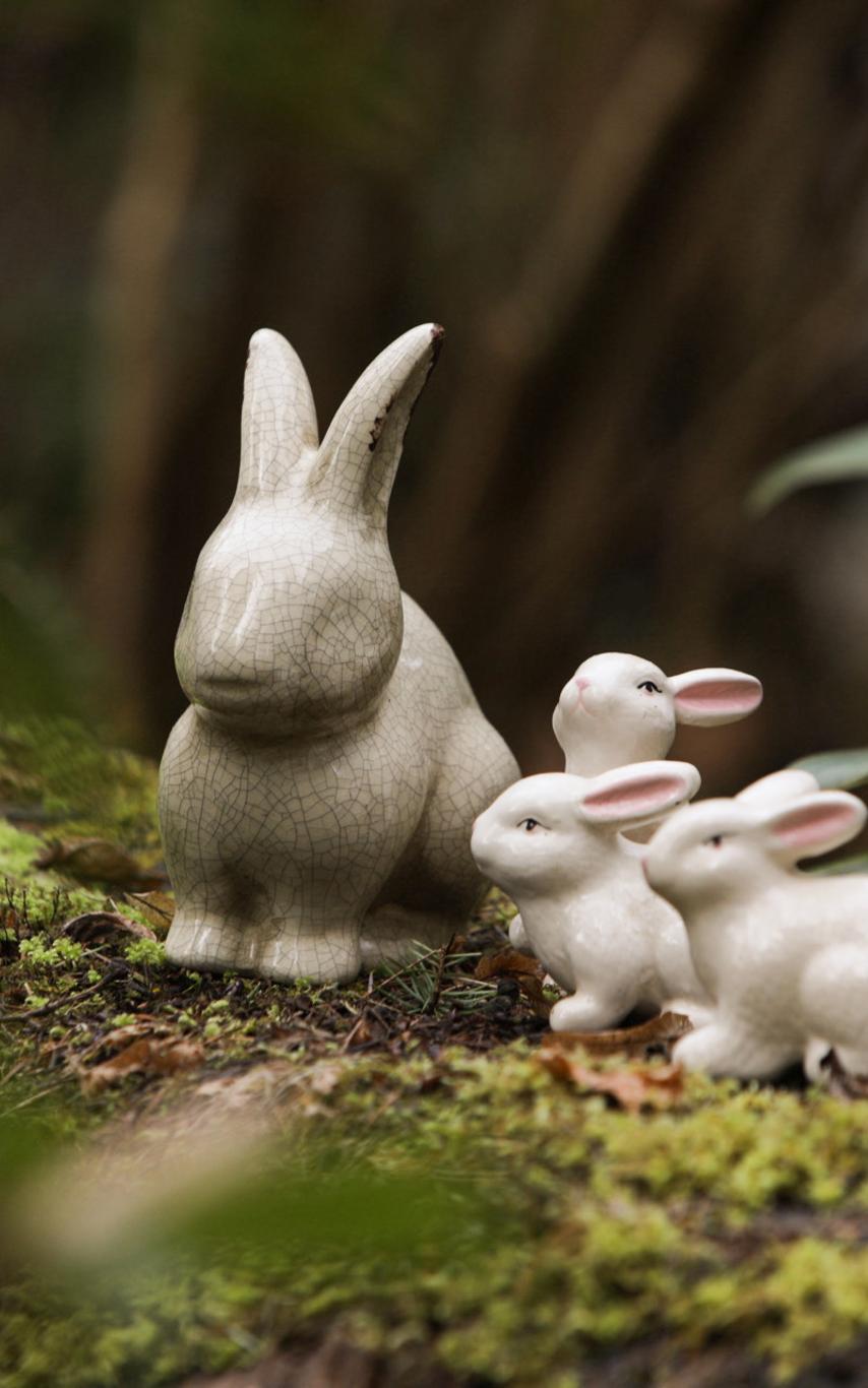 Decorative ceramic bunnies sitting on a mossy stump in the forest.